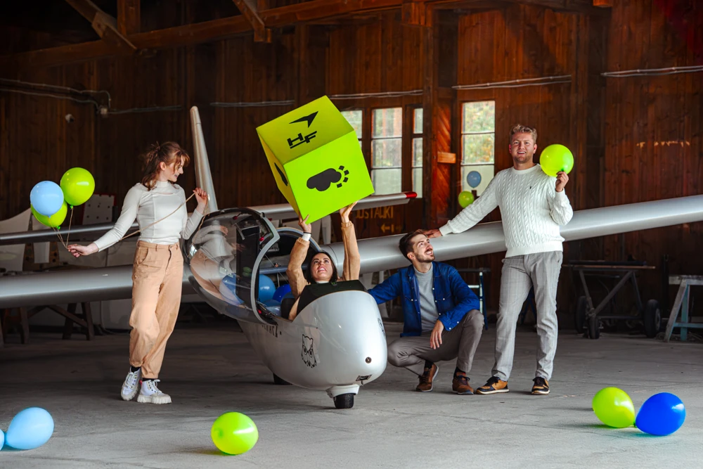 Sesja zdjęciowa High-Flyer — grupa ludzi z balonami i limonkowym pudełkiem przy szybowcu